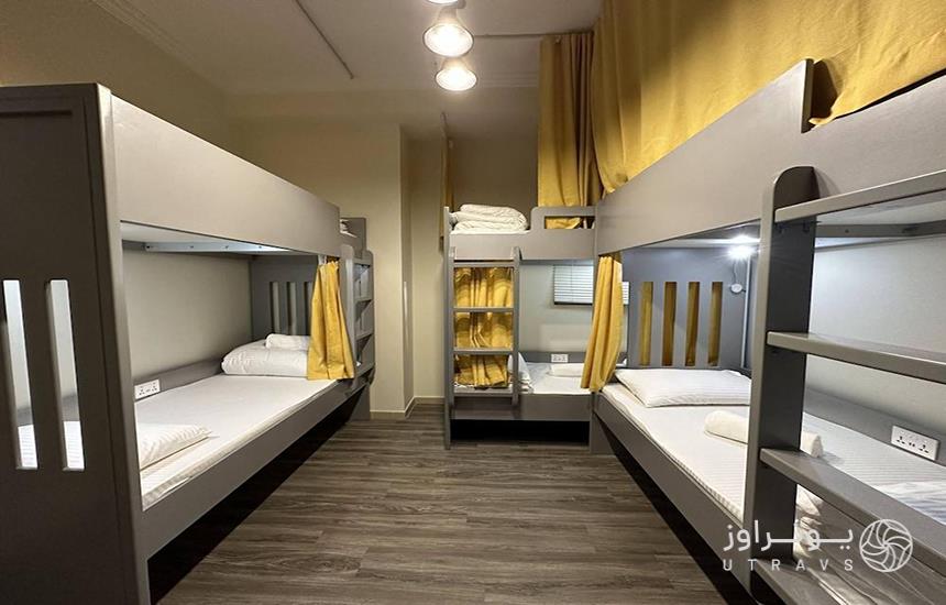 اتاقی در یک هاستل در دبی که چند تخت طوسی‌رنگ در آن قرار دارد که با پرده‌های زرد از هم جدا شده‌اند.